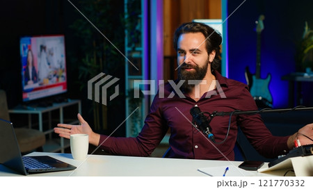 Playful online star using tech equipment to shoot video, doing frantic gesturing. Energetic content creator jumping on chair, having fun while filming vlog with professional mic in studio, camera A 121770332