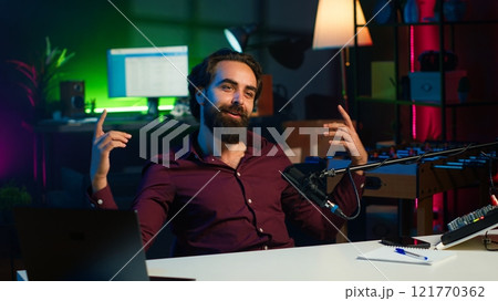 Playful internet star playing guitar in studio while shooting video. Energetic content creator playing musical instrument while filming vlog with professional mic in home studio, camera A 121770362