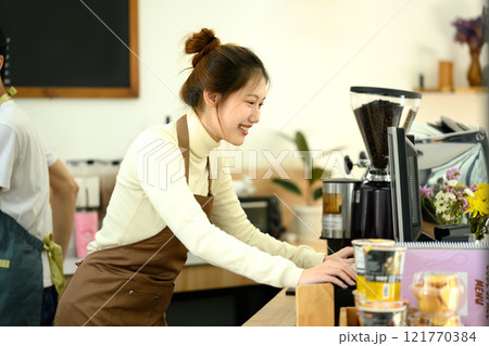 Smiling barista wearing apron working at the counter in a contemporary cafe 121770384