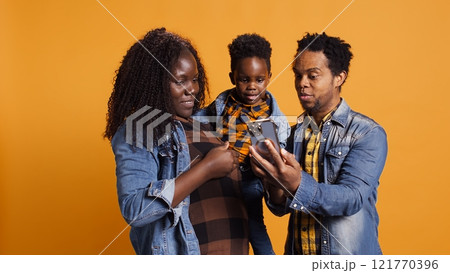 Cute happy family with a young kid take pictures on smartphone, carrying their son and sharing embrace in studio. African american parents feeling grateful for their toddler. Camera B. Cute happy family with a young kid take pictures on smartphone, carrying their son and sharing embrace in studio. African american parents feeling grateful for their toddler. Camera B. 121770396