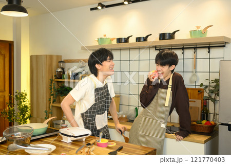 Joyful gay couple sharing a lighthearted moment in the kitchen while preparing food together. 121770403