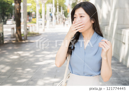 オフィス街で眠くてあくびをしているビジネスウーマン 121774445