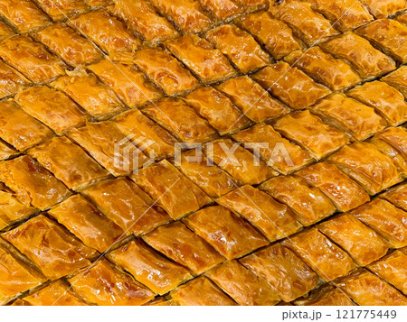 Solid background of freshly baked baklava laid out in rows, golden brown with syrup glaze, traditional Middle Eastern sweet pastry dessert, close up texture. Ramadan concept. 121775449
