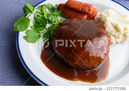 テーブルに置かれた、彩の良い野菜の付け合わせが添えられた美味しそうなハンバーグの盛られたお皿 121775588