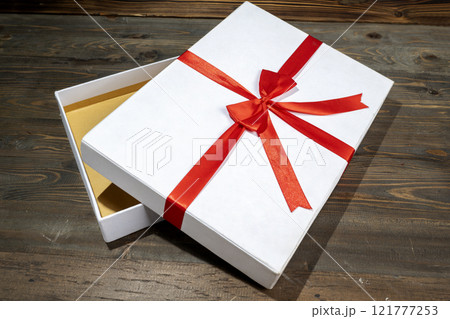 Opening a white gift box tied with a red ribbon on a wooden table Opening a white gift box tied with a red ribbon on a wooden table 121777253