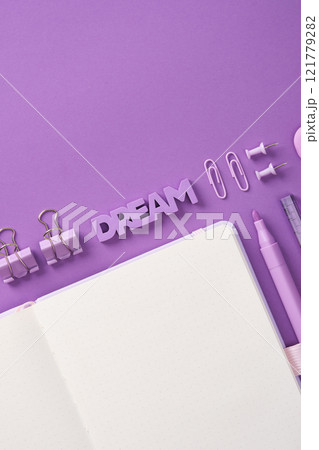 Minimalist pastel stationery flatlay with open notepad, eraser in the shape of the word Dream and stationery - pen, paper clips, clips and eraser on a lilac background. Place for your text. 121779282