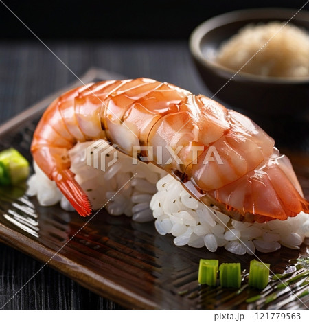 Fresh shrimp sushi on rice, garnished with green onion, served on black plate.  121779563