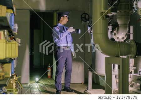 夜のビルを懐中電灯を持って警備する男性警備員　撮影協力：学校法人電波学園　東京電子専門学校 121779579