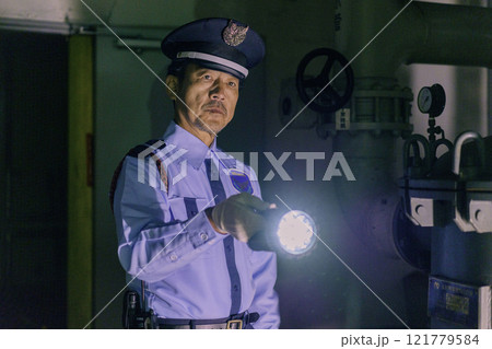 夜のビルを懐中電灯を持って警備する男性警備員　撮影協力：学校法人電波学園　東京電子専門学校 121779584