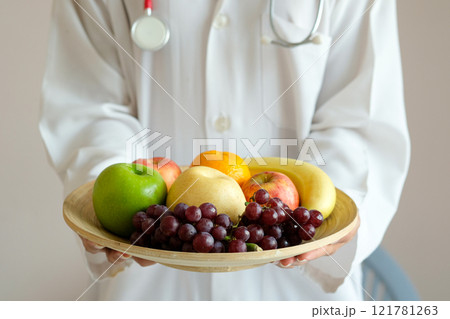 The hands of a healthy nutritionists, she holds a bowl with fruits, apples, grapes and avocados. 121781263