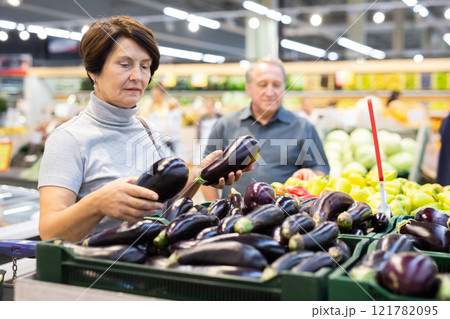 Elderly woman chooses eggplants in vegetable and fruit department Elderly woman chooses eggplants in vegetable and fruit department 121782095