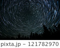 Star trails create mesmerizing circular patterns over a forest at night in a remote location 121782970