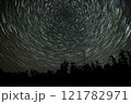Star trails create mesmerizing patterns above a dark forest at night 121782971