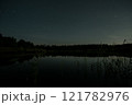 Night sky reflecting on tranquil waters surrounded by forest in a peaceful natural setting 121782976