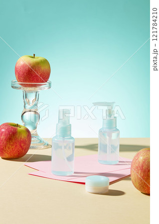 On a light blue backdrop An apple is positioned next to a mockup of blue beauty products on pink paper, placed on a yellow surface. Cosmetics advertising photo. On a light blue backdrop An apple is positioned next to a mockup of blue beauty products on pink paper, placed on a yellow surface. Cosmetics advertising photo. 121784210