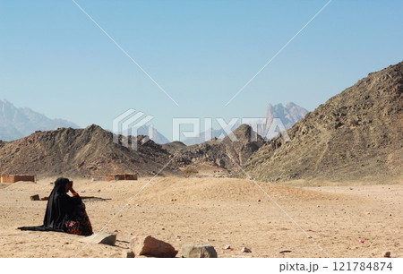 Bedouin woman in black paranja seating in the middle of rocky desert in Egypt. Bedouin woman in black paranja seating in the middle of rocky desert in Egypt. 121784874