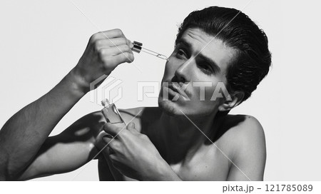 Man with smooth skin, applying serum with dropper against white background in black-and-white filter. Cosmetic, skin care product. Man with smooth skin, applying serum with dropper against white background in black-and-white filter. Cosmetic, skin care product. 121785089
