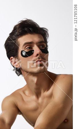 Man with smooth and moisturized skin, with black eye patches under his eyes looking to side against white studio background. Man with smooth and moisturized skin, with black eye patches under his eyes looking to side against white studio background. 121785108