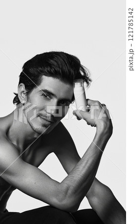 Handsome, smiling man sitting in casual pose and holding battle of cosmetic product for facial care against white background. 121785142