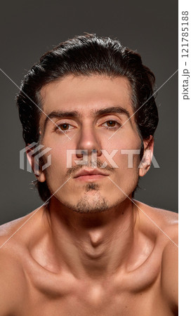 Close-up of handsome man staring straight into camera. His sharp features, well-groomed hair, and soft skin highlighted against dark background. Close-up of handsome man staring straight into camera. His sharp features, well-groomed hair, and soft skin highlighted against dark background. 121785188