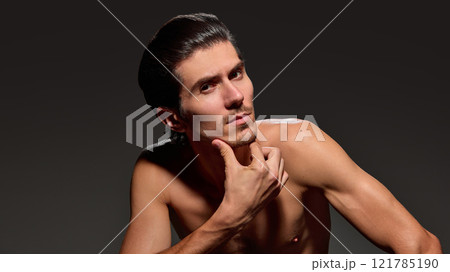 Handsome, stylish man resting his chin on his hand, creating inquisitive pose, highlights his focused expression against dark background. 121785190