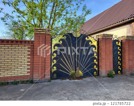 Brick fence with wrought iron gates in the shape of a peacock with red brick columns Brick fence with wrought iron gates in the shape of a peacock with red brick columns 121785722