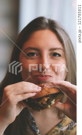 Close-up portrait of a woman in a fast food cafe eating a hamburger. Hungry woman eating a burger. Close-up portrait of a woman in a fast food cafe eating a hamburger. Hungry woman eating a burger. 121785811
