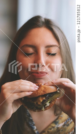 Close-up portrait of a woman in a fast food cafe eating a hamburger. Hungry woman eating a burger. Close-up portrait of a woman in a fast food cafe eating a hamburger. Hungry woman eating a burger. 121785812