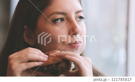 Close-up portrait of a woman in a fast food cafe eating a hamburger. Hungry woman eating a burger. 121785817