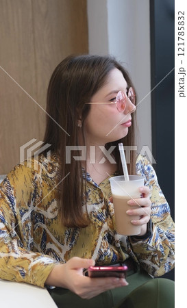Pretty brunette with phone in hands relaxing in cafe. Woman drinking coffee cocktail 121785832