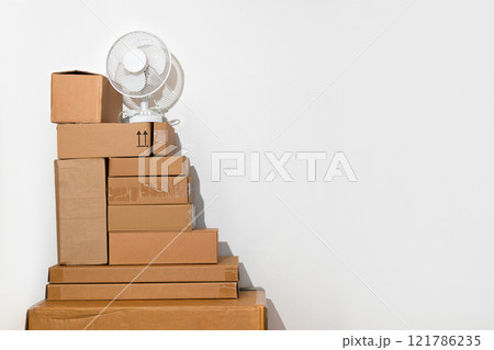 Creative minimalist image of stacked cardboard boxes with fan on a plain background, representing concepts of moving, storage, shipping, and organization Creative minimalist image of stacked cardboard boxes with fan on a plain background, representing concepts of moving, storage, shipping, and organization 121786235