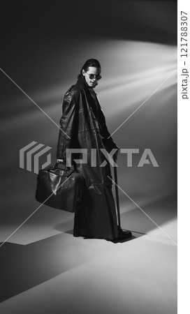 Monochrome, full length portrait of vampire wearing round glasses and leather coat poses holding bag and cane. Lord of darkness. 121788307