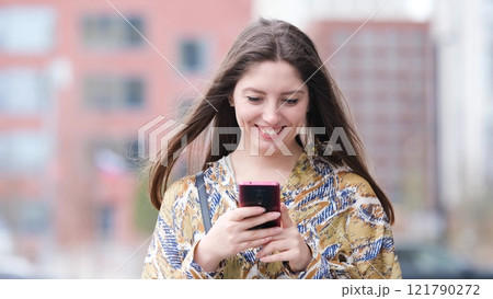 Beautiful woman with long blond hair holding mobile phone, looking at mobile phone screen, using smartphone apps. posing on street. Positive model smiling. She is standing with smartphone in hands on Beautiful woman with long blond hair holding mobile phone, looking at mobile phone screen, using smartphone apps. posing on street. Positive model smiling. She is standing with smartphone in hands on 121790272