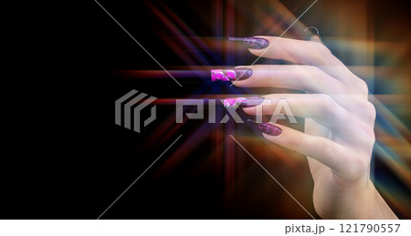A hand with a beautiful manicure in the rays of multi-colored optical light on a black background. Nail design. Extended nails. 121790557