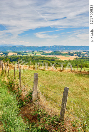 Countryside farm land with a fence on a blue cloudy sky background with copy space. Landscape of a sustainable agriculture farmland with hay like grass and trees in a green environment Countryside farm land with a fence on a blue cloudy sky background with copy space. Landscape of a sustainable agriculture farmland with hay like grass and trees in a green environment 121790938