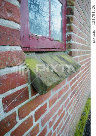 Old dirty window on a brick wall house or home. Ancient casement with red wood frame on a historic building with a clumpy paint texture. Exterior details of a windowsill in a traditional country town Old dirty window on a brick wall house or home. Ancient casement with red wood frame on a historic building with a clumpy paint texture. Exterior details of a windowsill in a traditional country town 121791326