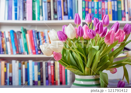 Fresh white and pink tulips in a vase with a shelf of library books in the background. Closeup of beautiful and colorful bunch of flowering plants in bloom. Vibrant bouquet to brighten a reading room 121791412