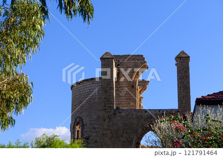 A historic stone tower rises against a clear blue sky surrounded by vibrant greenery in a peaceful setting 121791464