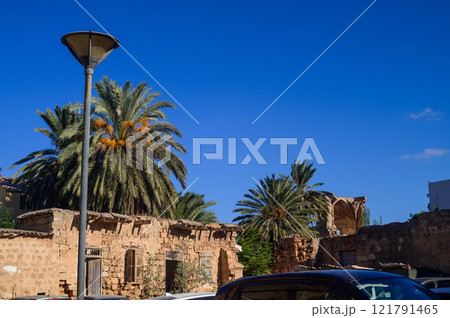 Old stone structures under a vibrant blue sky surrounded by lush palm trees during a sunny day 121791465