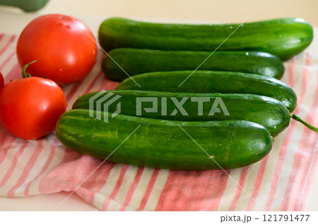 Fresh cucumbers and ripe tomatoes arranged on a striped kitchen towel in morning light 121791477