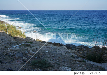 Waves crashing on rocky shoreline at a tranquil coastal area during the afternoon light. 121791500