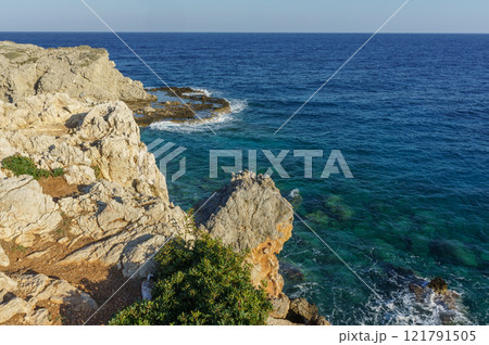 Serene coastal view from rocky cliffs overlooking the clear blue sea during a bright sunny day. Serene coastal view from rocky cliffs overlooking the clear blue sea during a bright sunny day. 121791505