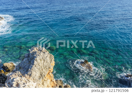 Vivid blue waters gently lapping against rocky shores at a tranquil seaside escape. Vivid blue waters gently lapping against rocky shores at a tranquil seaside escape. 121791506
