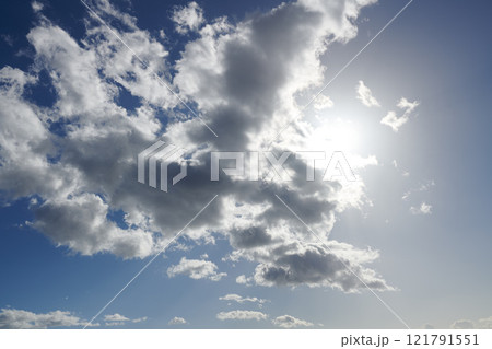 Clouds. Sun hiding behind clouds with blue sky. Beautiful sunshine from behind white and grey cumulus clouds at midday in summer. Serene view of natures outdoor beauty high in space. 121791551