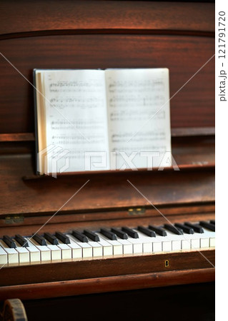 Old vintage piano with musical notes at a classical music festival. An antique wooden keyboard with a composition book ready for a melody to be created in an art gallery. A classic musical instrument Old vintage piano with musical notes at a classical music festival. An antique wooden keyboard with a composition book ready for a melody to be created in an art gallery. A classic musical instrument 121791720