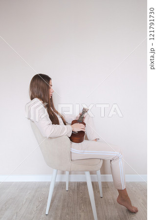 Woman with ukulele sitting on a chair. Woman with ukulele sitting on a chair. 121791730