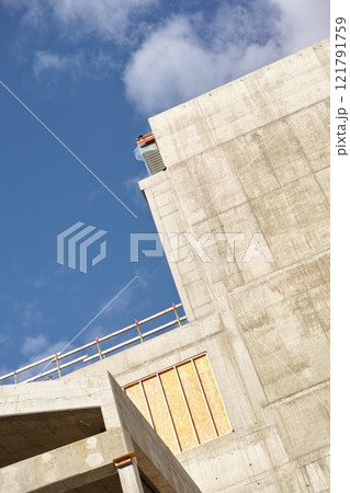 Exterior of a concrete building against a cloudy blue sky. Detail view of a tall residential or office building made of exposed concrete slabs. Construction phase of home remodel and addition Exterior of a concrete building against a cloudy blue sky. Detail view of a tall residential or office building made of exposed concrete slabs. Construction phase of home remodel and addition 121791759