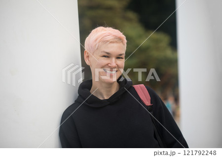 Happy woman with short hair smiling, standing and looking at camera, outdoors portrait 121792248