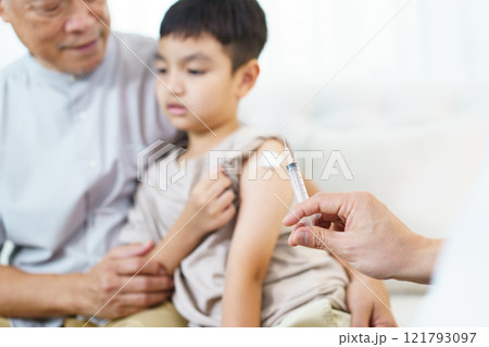 Asian little boy with grandfather in the doctor office in hospital is vaccinated by doctor. Doctor injecting a shot of vaccine on the boy's arm. Illness prevention concept. 121793097