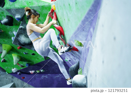 Asian sportswoman practices an indoor rock climbing wall. Asian sportswoman practices an indoor rock climbing wall. 121793251